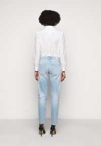Light blue denim jeans with a slim fit, high waist, and subtle fading. Paired with a white collared shirt and black high-heeled shoes.