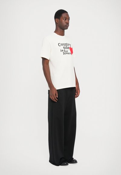 Witte kortemouw t-shirt met zwarte en rode tekst "Country side is for lovers." Gecombineerd met losse zwarte broek en zwarte schoenen.