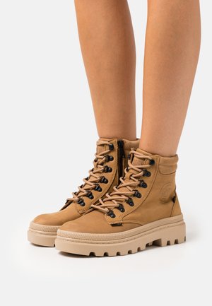 Bottines en cuir tan avec une finition texturée, œillets noirs, semelle épaisse beige, laçage à l'avant et fermeture éclair sur le côté pour un enfilage facile.