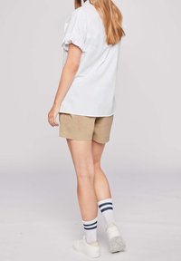 Vit kortärmad blus med volangdetaljer vid ärmarna, ihop med khaki-shorts. Vita strumpor med blå ränder och vita sneakers fulländar outfiten.