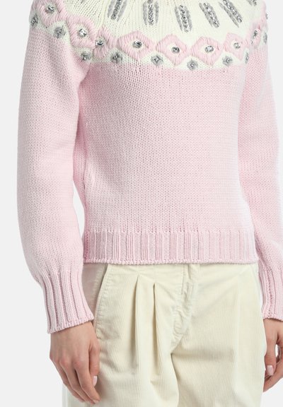 Jasnoróżowy sweter z dzianiny z białym i srebrnym wzorem diamentowym na klatce piersiowej, zestawiony z kremowymi plisowanymi spodniami sztruksowymi.