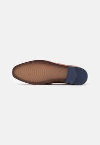 Semelle d'une chaussure habillée en cuir marron avec un bout pointu et un talon en caoutchouc bleu foncé, présentée sur un fond clair.