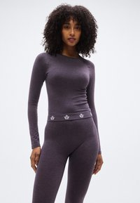 Μωβ εφαρμοστό μακρυμάνικο τοπ με ριμπ υφή και διακοσμητική λωρίδα με λογότυπο στη μέση, συνδυασμένο με αντίστοιχο κολάν.