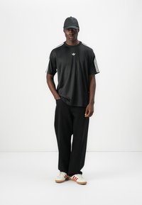 Μαύρο αθλητικό μπλουζάκι με τρεις λευκές ρίγες στα μανίκια και ένα μικρό λ ευκό λογότυπο. Συνδυασμένο με φαρδιά μαύρη παντελόνια και λευκά παπούτσια με κόκκινες ρίγες.