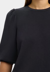 Mörkgrå kortärmad topp med rund halsringning och puffärmar, gjord av mjukt tyg med slät textur.