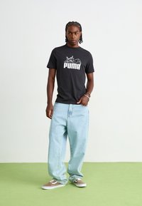 Sort bomulds t-shirt med hvid "PUMA" logo tryk, parret med lyseblå løse denim jeans og brune sneakers med hvide detaljer.