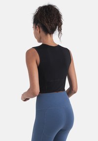 Musta hihaton lyhyt toppi, jossa on teksturoitu pinta, yhdistetty sinisiin korkeavyötäröisiin leggingsseihin, joissa on ompelukoristeita ja sileä materiaali.