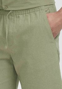 Lysegrønne linnedbukser med elastisk talje, sidelommer og en glat tekstur, der viser et afslappet og behageligt design.
