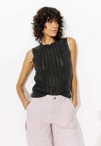 Un haut sans manches en tricot vert foncé avec des motifs texturés et un col rond, associé à un pantalon large rayé rose clair.