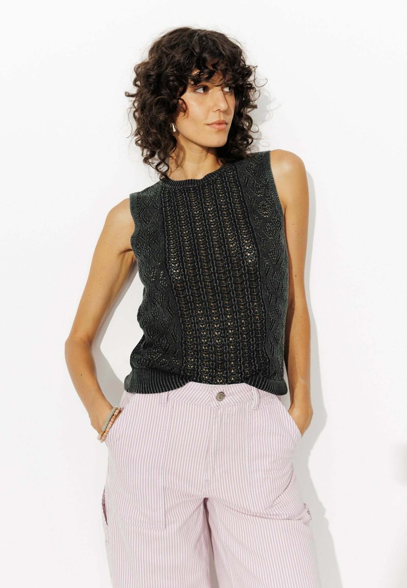 Un haut sans manches en tricot vert foncé avec des motifs texturés et un col rond, associé à un pantalon large rayé rose clair.