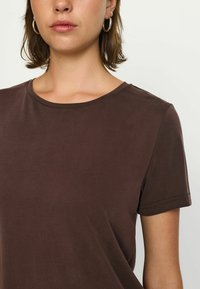 T-shirt marrone a maniche corte realizzato in tessuto morbido, con scollatura rotonda e superficie liscia. Nessun motivo o dettaglio visibile.