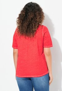 T-shirt rouge à manches courtes avec un tissu texturé, ourlet arrondi et coupe décontractée, vu de dos sur fond blanc.