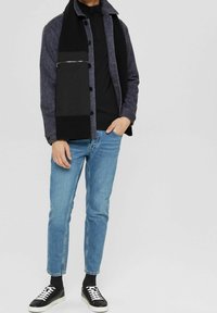 Košile-jacket v tmavě šedé a černé barvě, s kapsou na zip, spárovaná s černým topem, světle modrými džíny a černými teniskami s bílou podrážkou.