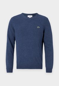 Mörkblå stickad tröja med långa ärmar, rund halsringning och en liten grön Lacoste-logotyp på vänster bröst. Mjuk textur, standard passform.