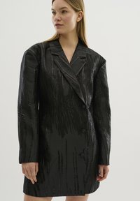 Schwarzes tailliertes Blazerkleid mit gerippter Texturierung, doppelter Knopfleiste und breiten Revers, ausgestattet mit dezenten Glanzelementen.