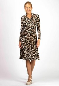 Klänning med leopardtryck, långa ärmar och omslagdesign. Tyget är smidigt; färgpaletten inkluderar beige, brunt och svart. Bärs med krämfärgade klackar.