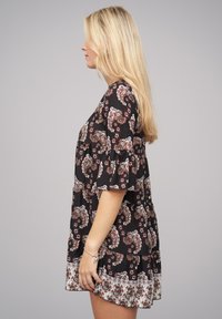 Musta mekko paisley-kuvioilla, röyhelöillä varustetut lyhyet hihat ja liehuva helma, jossa on valkoinen kukallinen alaosa. Sujuva kankaan rakenne.