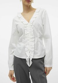 Witte katoenen blouse met een V-hals, ruches langs de middenlijn en lange mouwen. De stof lijkt glad met een lichte glans.