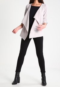 Světle šedý dřevěný blazer s tříčtvrtečními rukávy, v kombinaci s černým topem a černými slim džínami. Černé vysoké kotníkové boty na podpatku.