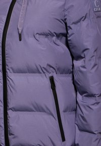 Doudoune lilas clair au design matelassé, dotée d'une fermeture éclair noire et d'accents de poche, fabriquée en matériau lisse et résistant à l'eau.