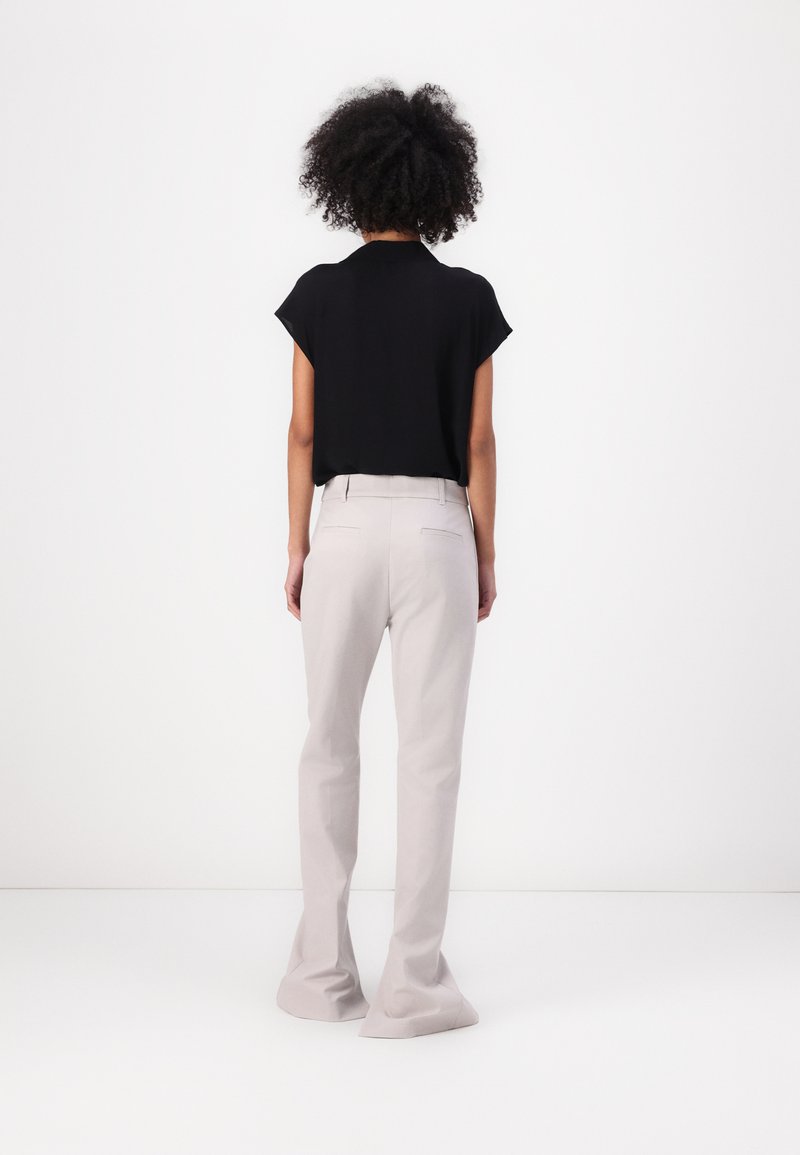 Haut noir à manches courtes et pantalon clair ajusté gris. Le haut a une coupe ample ; le pantalon a une coupe droite avec des ourlets évasés.