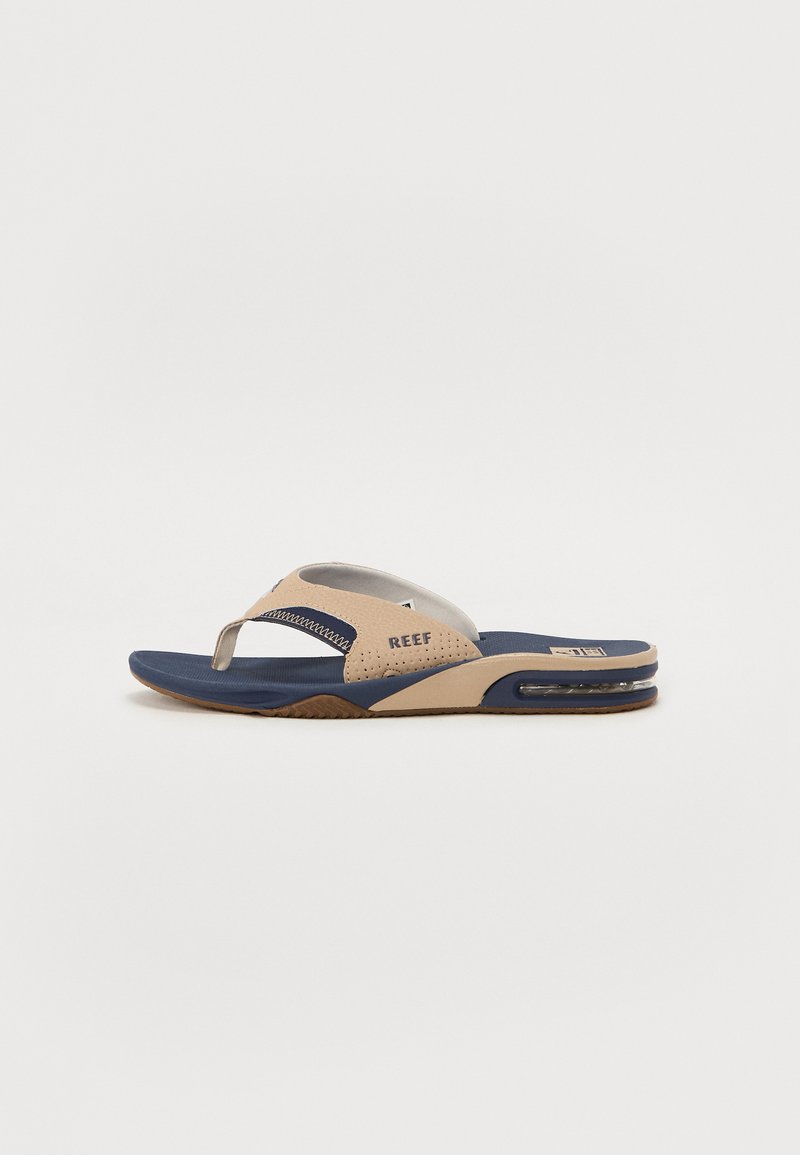 Lichtbeige slippers met een marineblauwe zool, voorzien van een gevoerde band, ventilatiegaten en een zichtbare luchtkussenelement.