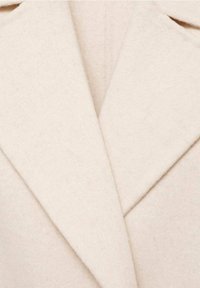 Gros plan sur les revers d’un manteau en laine beige avec un tissu doux et texturé et un col cranté classique.