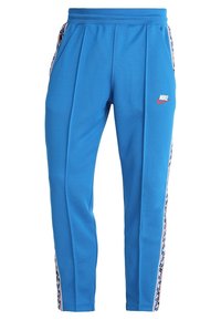 Modré tepláky Nike s elastickým pasem, bočními kapsami a vzorovanou lemovkou podél vnějších stehenních švů, s logem Nike na stehně.