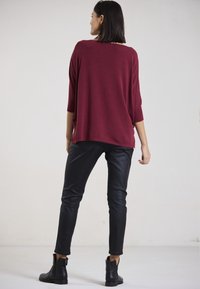 Burgunderfarbener, übergroßer Strickpullover mit Dreiviertelärmeln, kombiniert mit figurbetonten schwarzen Kunstlederhosen und schwarzen Ankle Boots.
