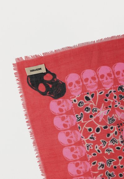 Κόκκινο κασκόλ με ροζ κρανία που σχηματίζουν ένα περίγραμμα και ένα μεγάλο μαύρο κρανίο κοντά στην ετικέτα που γράφει «Zadig & Voltaire», με κρόσσια στις άκρες.