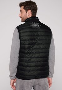 Gilet puffy nero con trapuntatura orizzontale, colletto alto e maniche di maglione grigie. Presenta testo stampato sul retro.