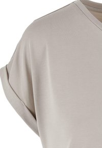 Ljusgrå kortärmad T-shirt med V-ringning och mjuk, ribbad textur. Har uppvikt ärmar och en avslappnad passform, tillverkad av lätt tyg.