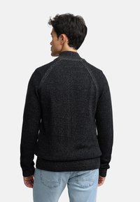 Sort struktureret sweater med høj krave og raglanærmer. Har ribbet kant og manchetter, med let spraglet detaljering over hele. 
