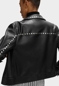 Zwarte leren jas met zilverkleurige studs langs de schouders en mouwen. Het ontwerp is getailleerd met een gladde textuur en een geribbelde kraag.