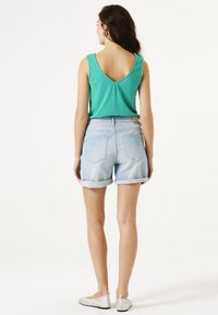 Top azul turquesa sin mangas con un diseño en V en la espalda, combinado con pantalones cortos de denim azul claro, doblados en el dobladillo. Corte holgado y tela texturizada. Planas plateadas.