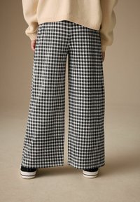 Hose mit weitem Bein aus Stoff mit schwarz-weißem Karo-Muster. Verfügt über seitliche Schlitze am Saum und ist mit schwarzen Turnschuhen kombiniert.