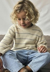 Cremig gestreifter Strickpullover mit rundem Ausschnitt und gerippten Bündchen, kombiniert mit hellblauen lässigen Denim-Jeans. Weiche Texturen und lockere Passform.