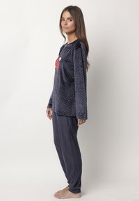 Conjunto de pijama de felpa suave de color azul marino, con mangas largas y pantalones. La parte superior presenta lunares blancos y un diseño gráfico rojo en el pecho.