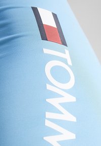 Lichtblauwe sportleggings met een opvallende witte "TOMMY" tekst en een klein rood, wit en blauw vlaglogo in de bovenste sectie.