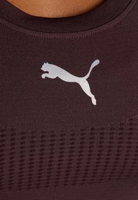 Viininpunainen urheilutoppi, jossa on ribbattu pinta, pyöreä pääntie ja näkyvästi esillä oleva heijastava hopeinen Puma-logo.