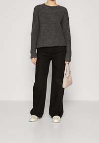 Grau gestrickter Pullover, locker sitzend, schwarze weite Hosen mit dezentem Glitzereffekt, cremefarbene Sneaker und eine kleine beigefarbene Handtasche. Einfaches Design, strukturierter Strick.