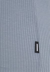 Gros plan sur un tissu gris à côtes avec une petite étiquette rectangulaire noire et blanche cousue près d'une couture.