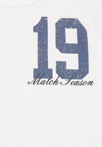 Biela látka s veľkým, vyblednutým modrým číslom "19" a čiernym kurzívnym textom "Match Season" pod číslom.