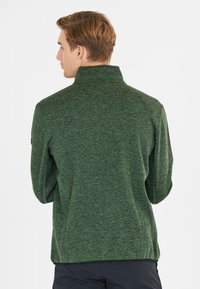 Grøn, struktureret zip-up jakke med høj krave, der har et let meleret mønster og en tætsiddende pasform.