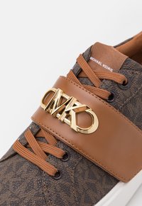 Baskets marron à motif foncé avec lacets marron, une large bande avec le logo doré « MK » et « Michael Kors » sur la languette.