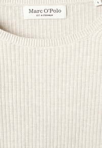 Pull en tricot beige clair avec une texture côtelée, doté d'un col rond et d'une étiquette "Marc O'Polo" au niveau du col. Taille S.