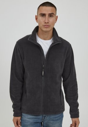 Chaqueta de forro polar gris con cuello alto, cremallera frontal y bolsillos laterales. Textura suave y ajuste ceñido, combinados con un estilo casual para superponer.