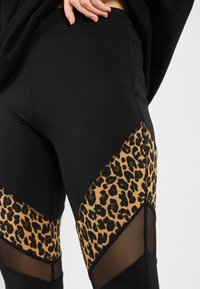 Leggings neri con un pannello a stampa leopardata a forma di diamante, con dettagli in rete vicino alle ginocchia e tessuto liscio ed elasticizzato.