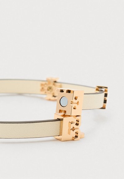 Κρέμα δερμάτινη ζώνη με χρυσή τετράγωνη αγκράφα που διαθέτει ανάγλυφες διακοσμητικές λεπτομέρειες και μαγνητική κλείσιμο.