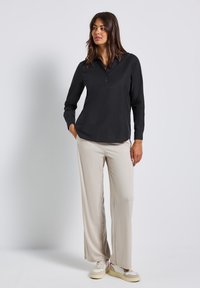 Blusa nera a maniche lunghe con colletto e bottoni abbinata a pantaloni beige a gamba larga e sneakers bianche. Tessuto liscio con una vestibilità rilassata.